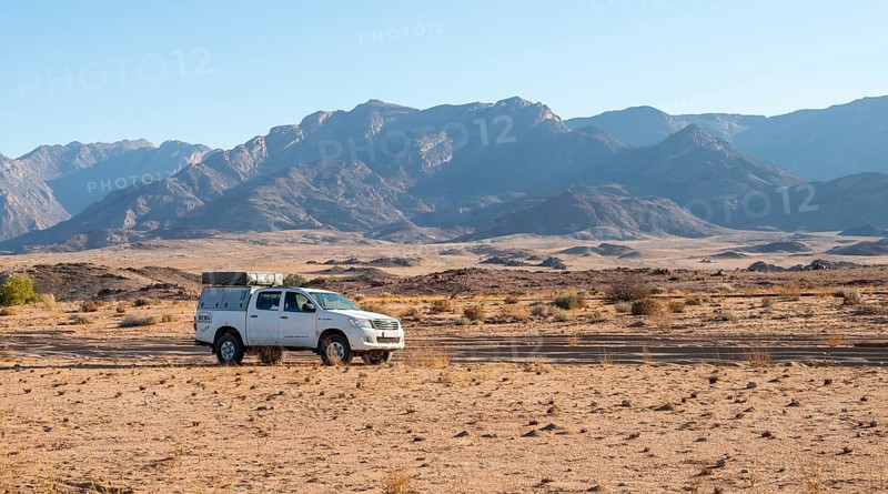 Tourist with off-road car on a sandy track, rock formation, Brandberg, Damaraland, Namibia