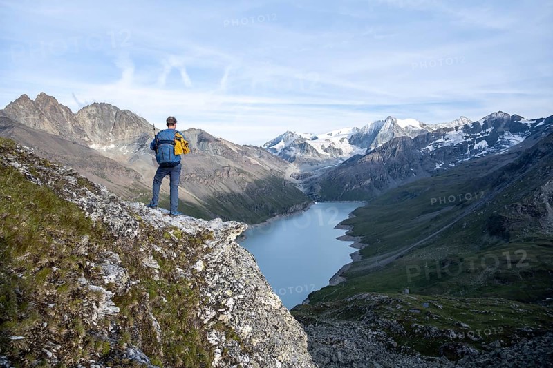 Mountaineer on the summit of Mont de la Blana, view of a blue mountain lake, Lac des Dix reservoir, behind mountain peak Mont Blanc de Cheilon with glacier, Hérménence, Valais Alps, Valais, Switzerland