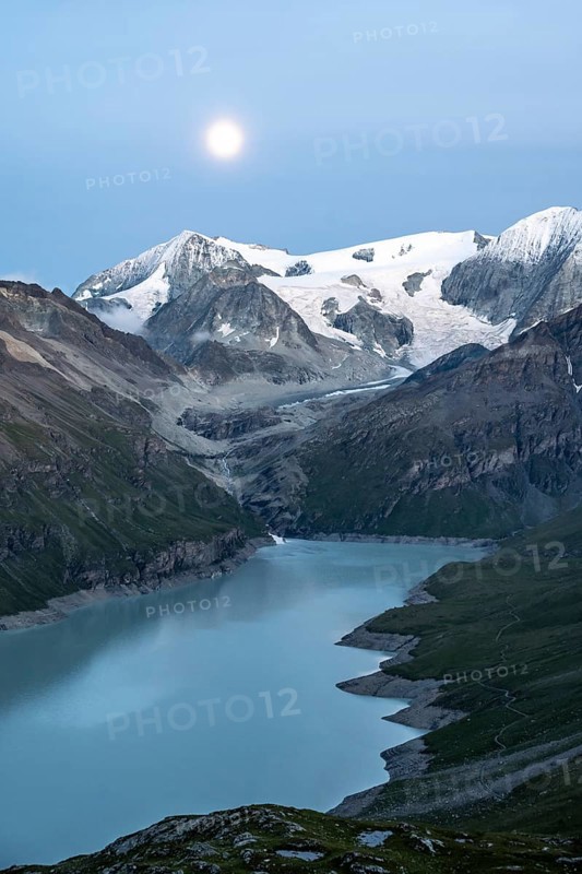 Mountain landscape with turquoise blue reservoir Lac des Dix and summit Mont Blanc de Cheilon, evening mood, moon stands above mountain peaks at the blue hour, Hérménence, Valais Alps, Valais, Switzerland