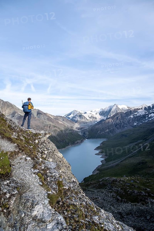Mountaineer on the summit of Mont de la Blana, view of a blue mountain lake, Lac des Dix reservoir, behind mountain peak Mont Blanc de Cheilon with glacier, Hérménence, Valais Alps, Valais, Switzerland