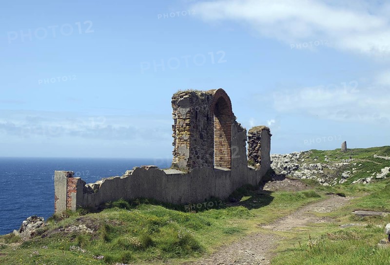 A coastal ruin with a view of the blue sea and green meadows under a cloudy sky, Mining, Botallack, Cornwall, United Kingdom