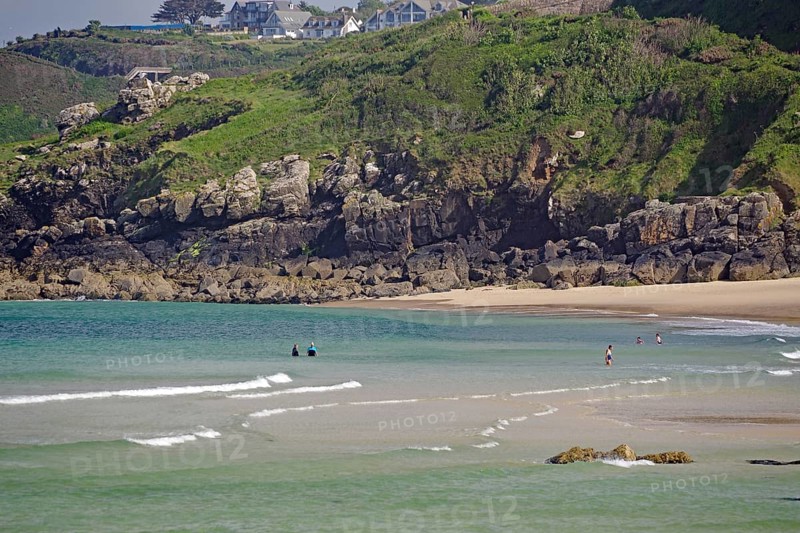 Small waves rolling towards a sandy beach with rocks, people enjoying the water, St Ives, Cornwall, England, United Kingdom
