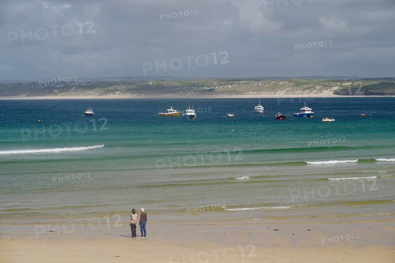 Boats anchored on calm waters off a wide, deserted sandy beach, St Ives, Cornwall, England, United Kingdom