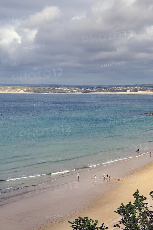 Several people walking on a quiet sandy beach, the sea under a cloudy sky, St Ives, Cornwall, England, United Kingdom