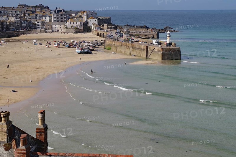 Coastal town with harbour and lighthouse, boats on the beach and gentle waves in the blue sea, tides, St Ives, Cornwall, England, Great Britain