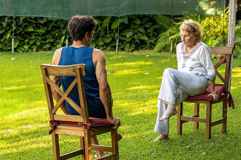 Senior woman and her physiotherapist are sitting on chairs in a garden, practicing rehabilitation exercises to improve mobility and well-being