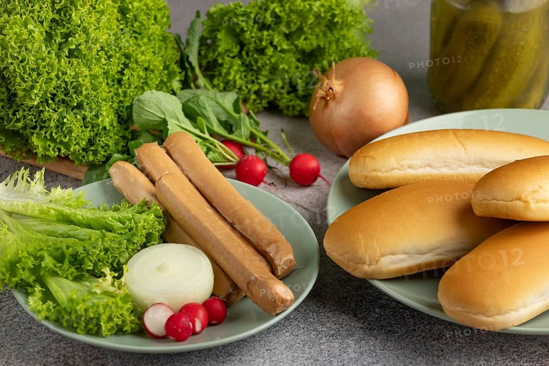 Various ingredients on plates, including salad, sausages and bread rolls