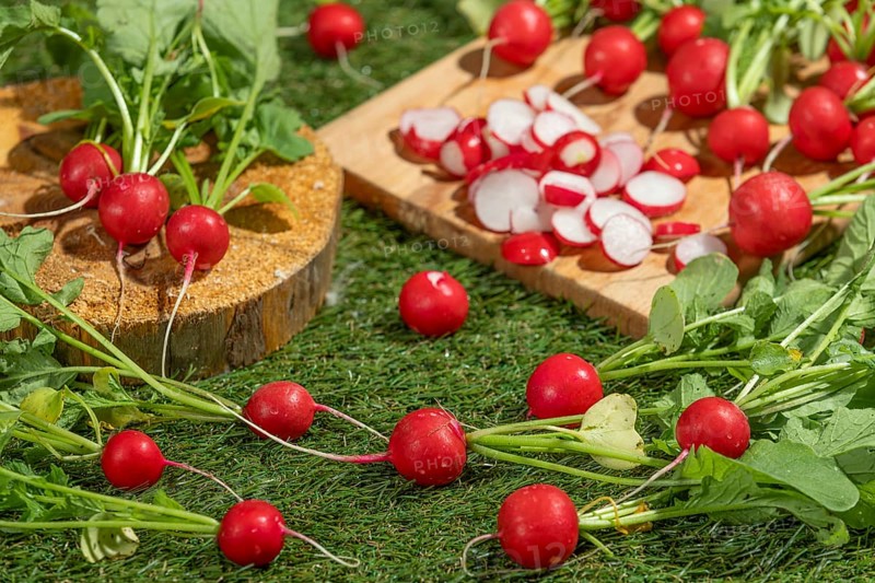 Fresh radishes, partly sliced, arranged on a wooden board on a green meadow