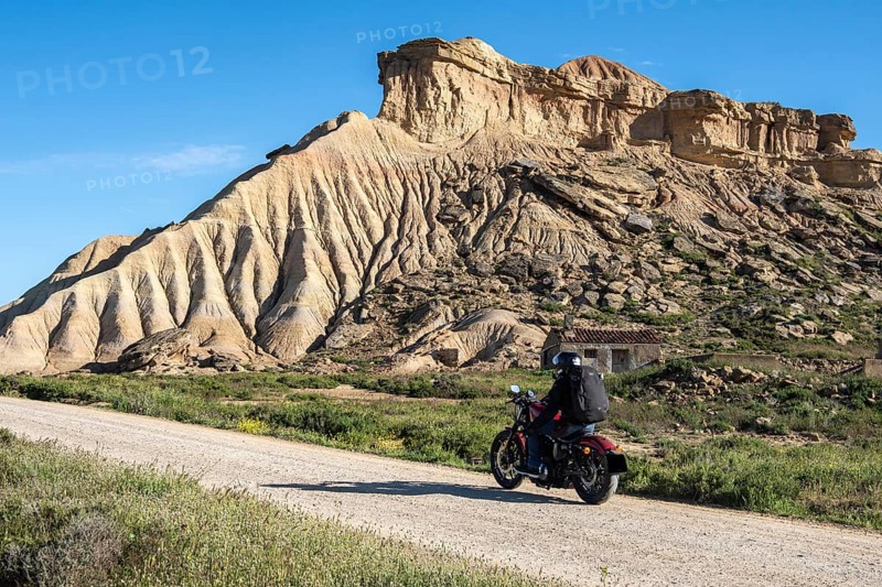 Biker riding motorcycle, gravel road, colorful rock formation, semi-desert, Bardena Blanca area, Bardenas Reales Nature Park, Navarre, Spain