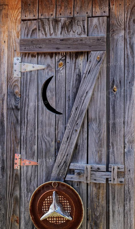Weathered wood door to outhouse with moon cut-out
