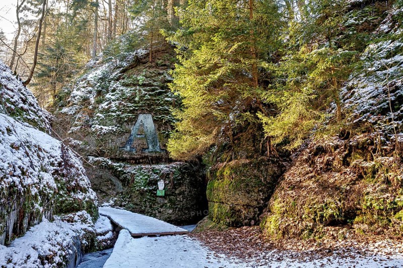 Snow-covered forest path leads through a shady gorge with rock-like formations and moss, The Dragon Gorge near Eisenach in Thuringia
