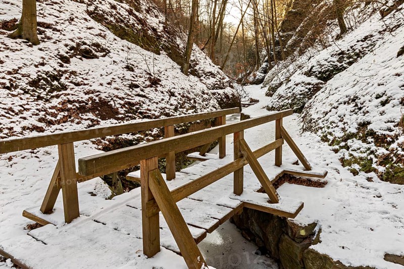 Narrow wooden bridge over a frozen stream in a snowy forest gorge at sunset, The Dragon Gorge near Eisenach in Thuringia
