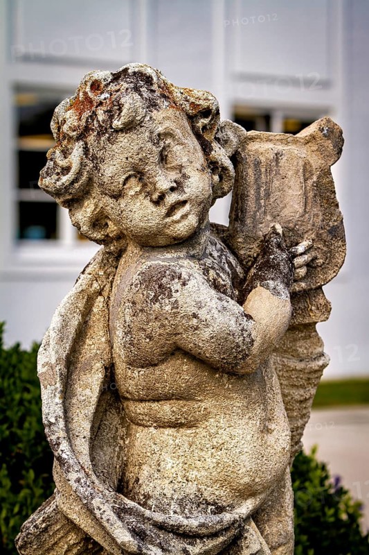 Weathered stone statue of an angel child with wings and background outdoors, stone statues in the town of Kempten im Allgäu