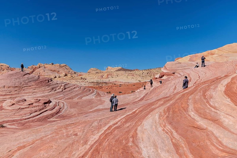 Hikers on a layered sandstone rock formation in the Fire Wave area of Valley of Fire State Park near Overton, Nevada