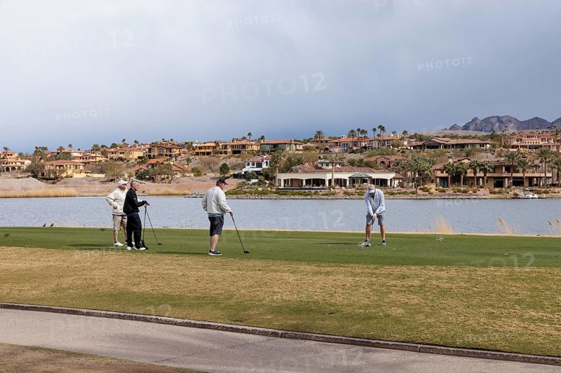 Foursome of senior golfers teeing off while playing on a golf course along the shoreline of Las Vegas Wash at Lake Las Vegas in Henderson, Nevada, USA