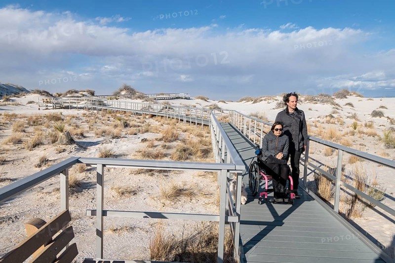 Man and handicapped woman in wheelchair stroll down the Interdune Boardwalk with their ped dog at White Sands Nationl Park near Alamogordo, New Mexico