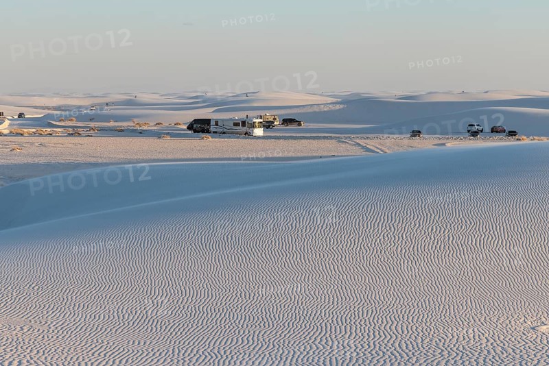 Cars and RVs in a parking area behind a rippled white gypsum sand dune at White Sands National Park in Alamogordo, New Mexico, USA