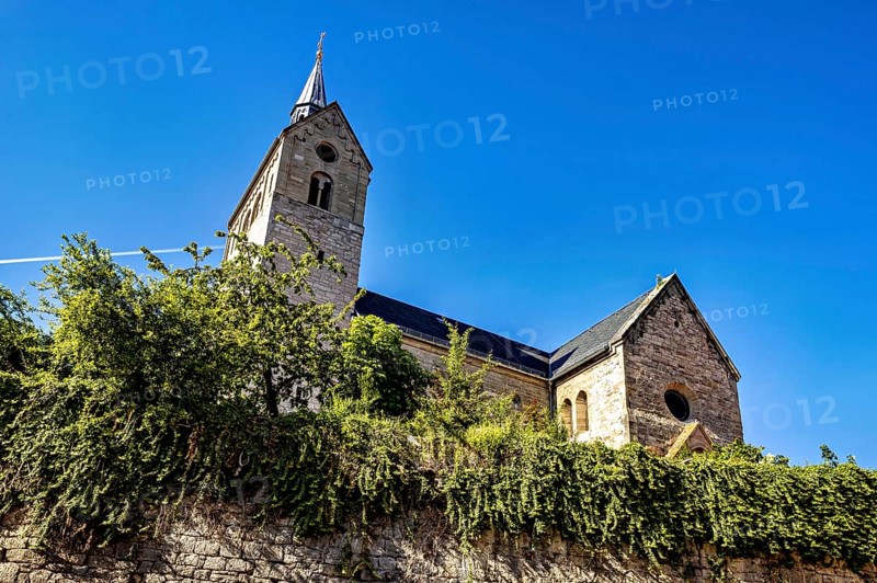 Historic church with striking stone architecture and vegetation in the foreground under a blue sky, The church of the town of Treffurt in Thuringia