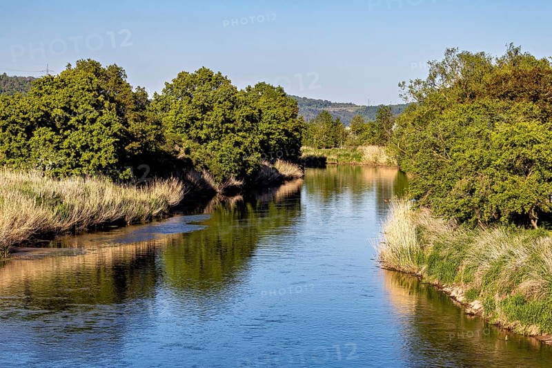 A quiet river, lined with dense trees, stretches through a peaceful landscape, Normannstein Castle near Treffurt in Thuringia