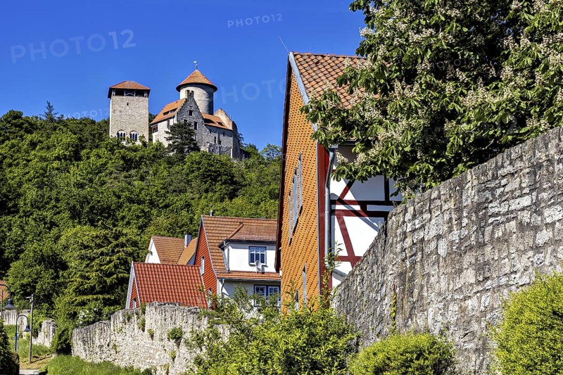 Half-timbered houses in a village in front of an imposing towering castle on a green hill, Normannstein Castle near Treffurt in Thuringia