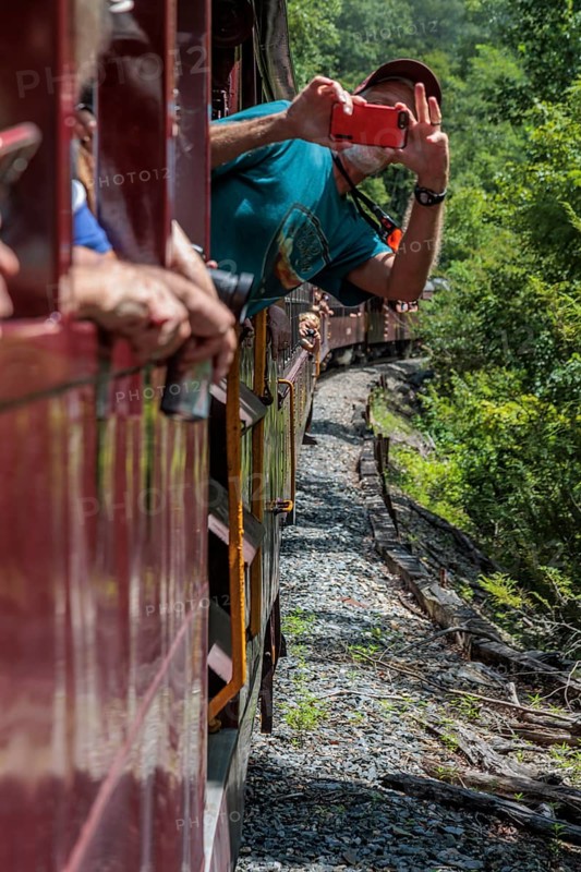 Man leaning out of the window of an open air train car of the Great Smoky Mountains Railroad to take a picture on an excursion from Bryson City, North Carolina