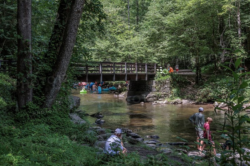 Visitors cross Trail Bridge to get upstream with inflatables for tubing along Deep Creek in the Smoky Mountains near Bryson City, North Carolina, USA