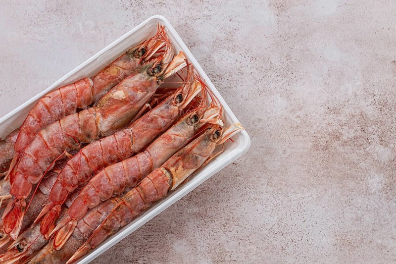 Fresh frozen Argentine shrimp, laid out in a container, top view, no people