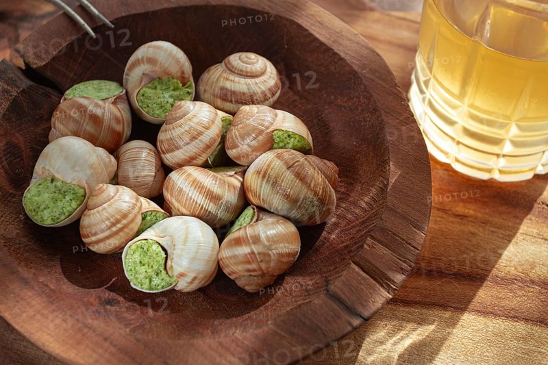 Snails cooked with herb oil on a wooden plate, served with white wine, natural light, no people
