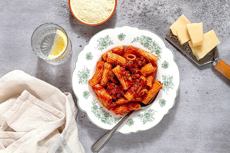 Rigatoni pasta with meat sauce and parmesan cheese on a light table, top view, homemade, no people