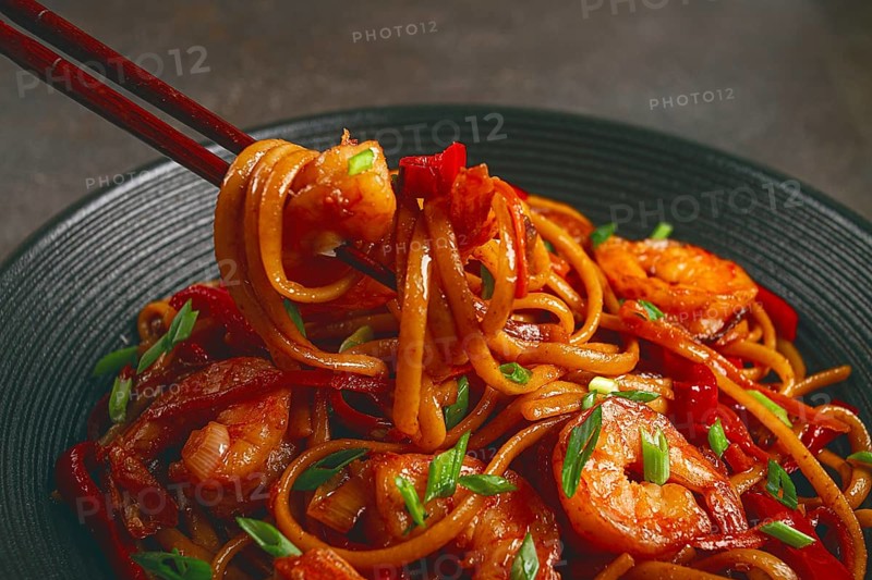 Udon stir-fry shrimp noodles with red bell pepper and green onion, served in a black bowl, with chopsticks, dark background