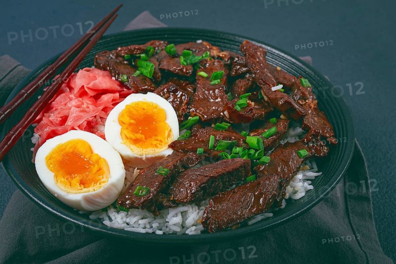 Udon Japanese beef with rice, pickled ginger, boiled egg slice, garnished with green onions, in a black bowl, with chopsticks