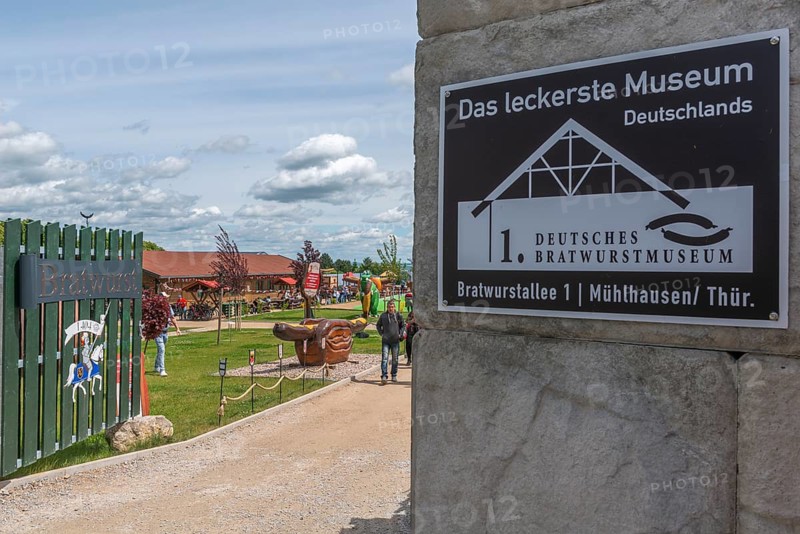 First German Bratwurst Museum, Bratwurstallee 1, Mühlhausen, entrance with inscription, medieval knight figure with the year 1404, museum grounds outside, giant Thuringian bratwurst in bread with mustard, many people, sunshine, Thuringia, Germany
