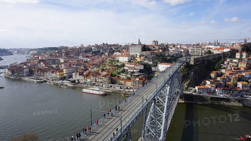 View from above of the metal bridge Ponte dom Luis across the Douro in Porto of a city with bridge and river under a blue sky and boats on the shore, Porto, Portugal