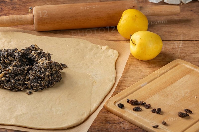 Rolled dough with poppy seeds and raisins on top, apple and rolling pin next to it