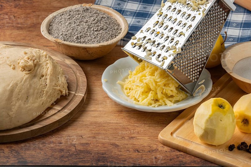 Grated apples and poppy seeds next to dough on rustic table