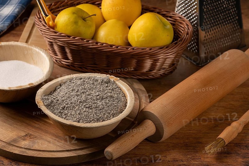 Basket with apples, bowl with poppy seeds and rolling pin on a rustic wooden table