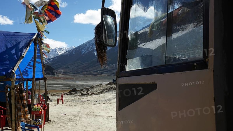 A bus and a colorful tent with pennants against a mountain backdrop, snack at a kiosk on a plateau in the Himalayas, trekking in Ladakh, Himalayas, India