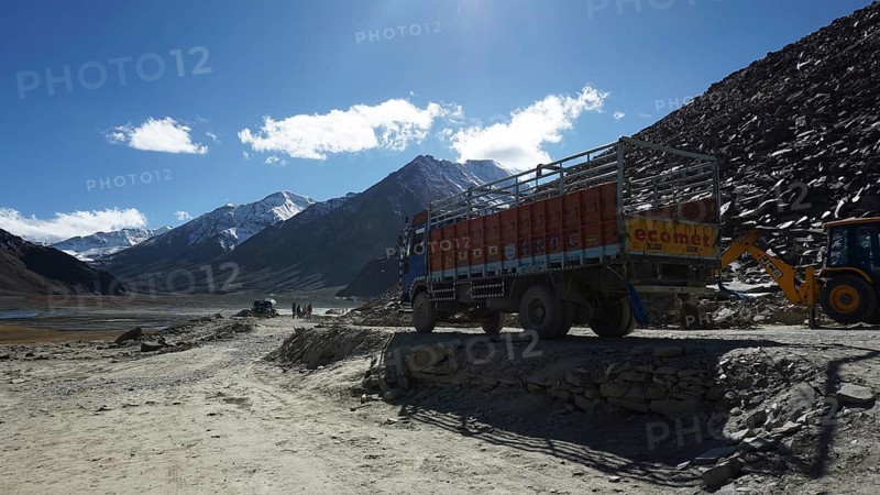 A truck parks on a mountain road with construction sites and mountains in the background, trekking in Ladakh, Himalayas, India