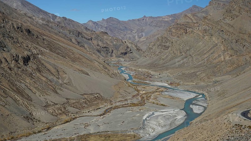 Shimmering blue Indus meanders through a barren valley under a blue sky, trekking in Ladakh, Himalayas, India