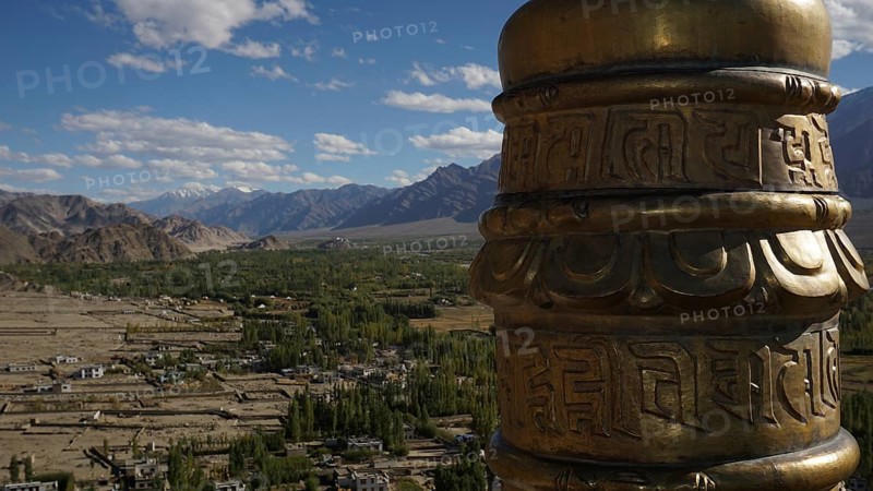Detail of a golden prayer wheel against the backdrop of a vast mountain landscape, view of the surrounding countryside from a Buddhist monastery, trekking in Ladakh, Himalayas, India