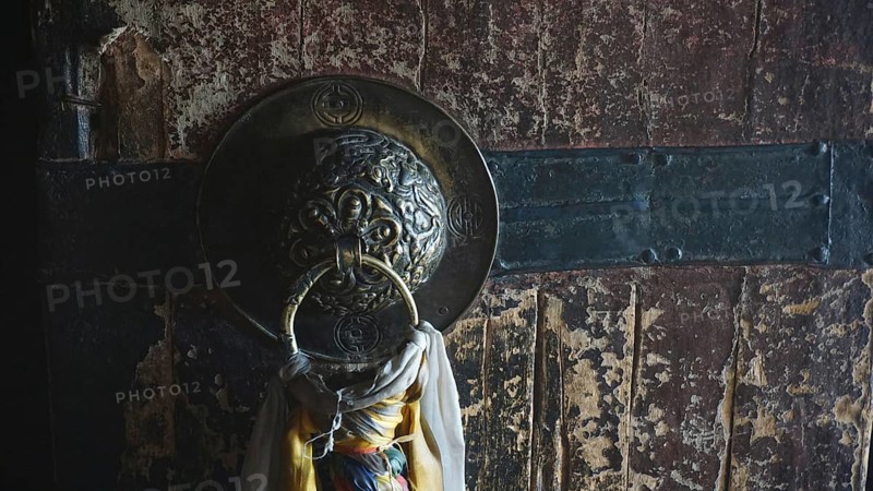 Detail of an old wooden door of a Buddhist monastery with metal ring and rope, surrounded by a dark, textured surface, trekking in Ladakh, Himalayas, India