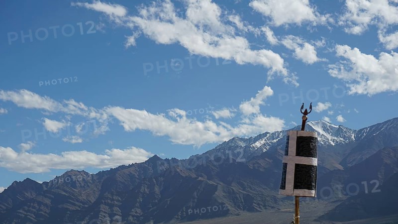 Mountain landscape with blue sky and clouds, flag in the foreground, trekking in Ladakh, Himalayas, India