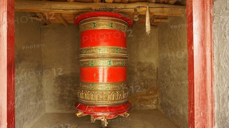 A large red prayer wheel decorated with decoration in a temple-like room, trekking in Ladakh, Himalayas, India