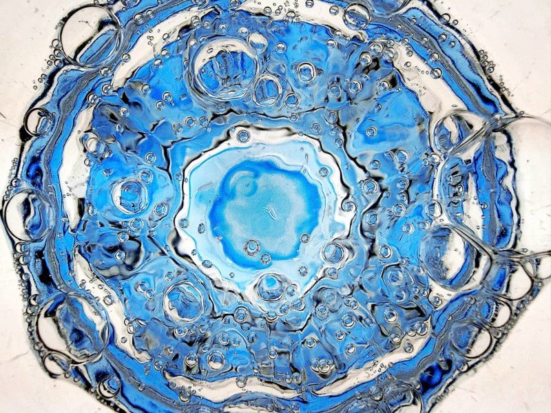 Rising carbon dioxide bubbles in a full water glass with a blue bottom seen from above, detail, Witten, North Rhine-Westphalia, Germany