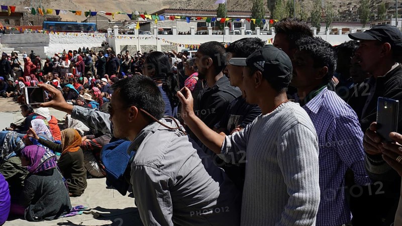 A crowd films an outdoor festival with smartphones, colorful details in the background, Leh, trekking in Ladakh, Himalayas, India