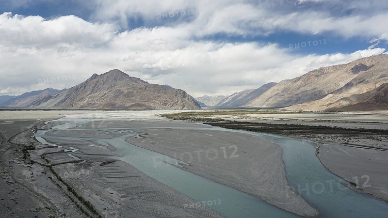 Extensive river landscape on the Indus with mountains in the background under a cloud cover, trekking in Ladakh, Himalayas, India