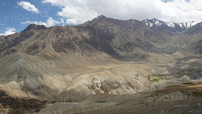 Dramatic mountain landscape with diverse rock formations, snow-capped peaks under a cloudy sky, trekking in Ladakh, Himalayas, India