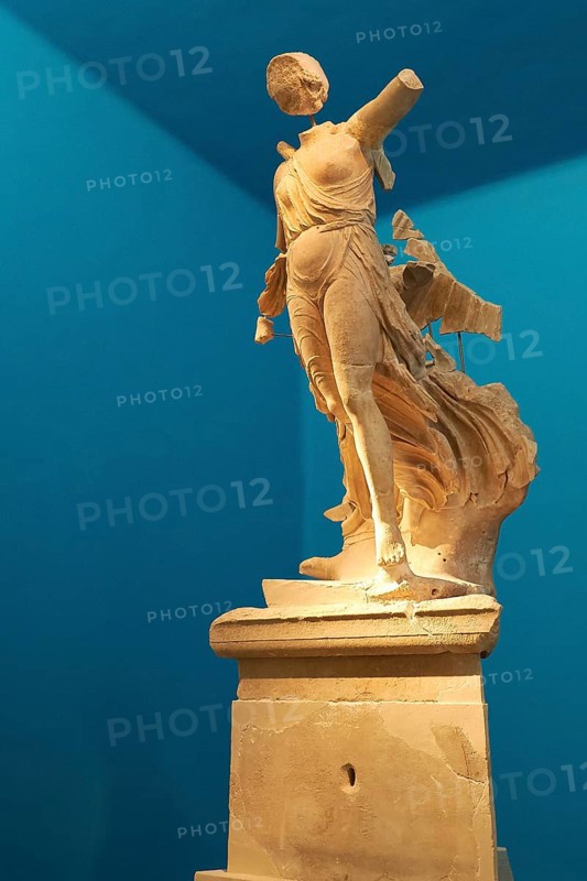 The Nike of Paionios, statue of the goddess of victory Nike from Parisian marble, fragment of an ancient female marble statue in dynamic pose against a blue background, Olympia Archaeological Museum, Ancient Olympia, Olympia, Peloponnese, Greece