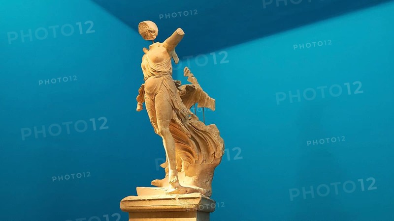 The Nike of Paionios, statue of the goddess of victory Nike from Parisian marble, fragment of an ancient female marble statue in dynamic pose against a blue background, Olympia Archaeological Museum, Ancient Olympia, Olympia, Peloponnese, Greece