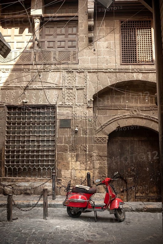 Cairo, Egypt. July 7th 2024 A cool looking red scooter parked in front of typical Egyptian architecture of the historical Islamic quarter of Cairo, ancient capital of Egypt